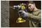 A man uses a yellow power drill to make a hole in a concrete wall. He wears safety glasses and gloves, focusing intently on the task.