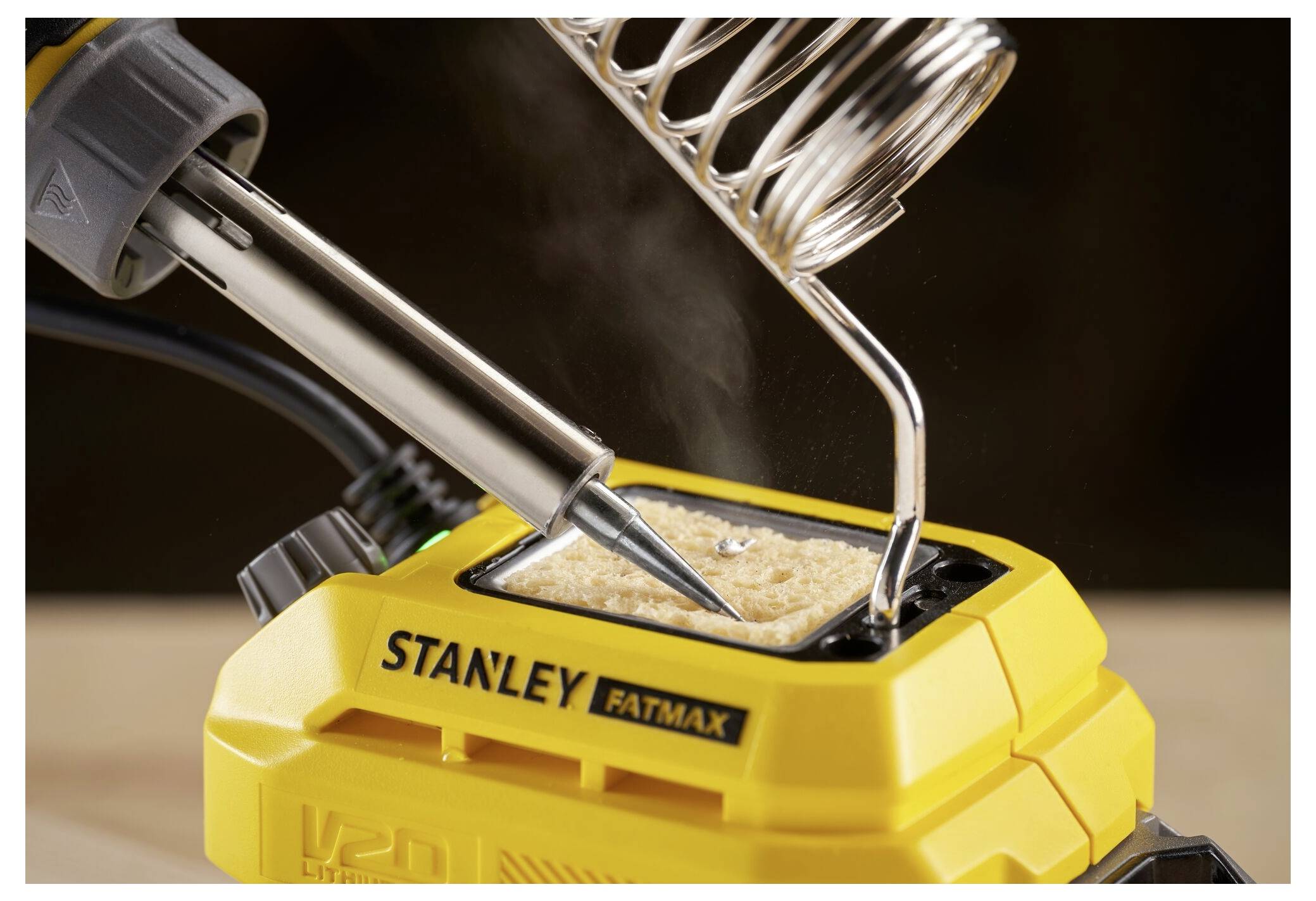 A yellow Stanley FatMax soldering iron kit with a hot soldering iron placed in its holder, emitting a slight wisp of smoke.