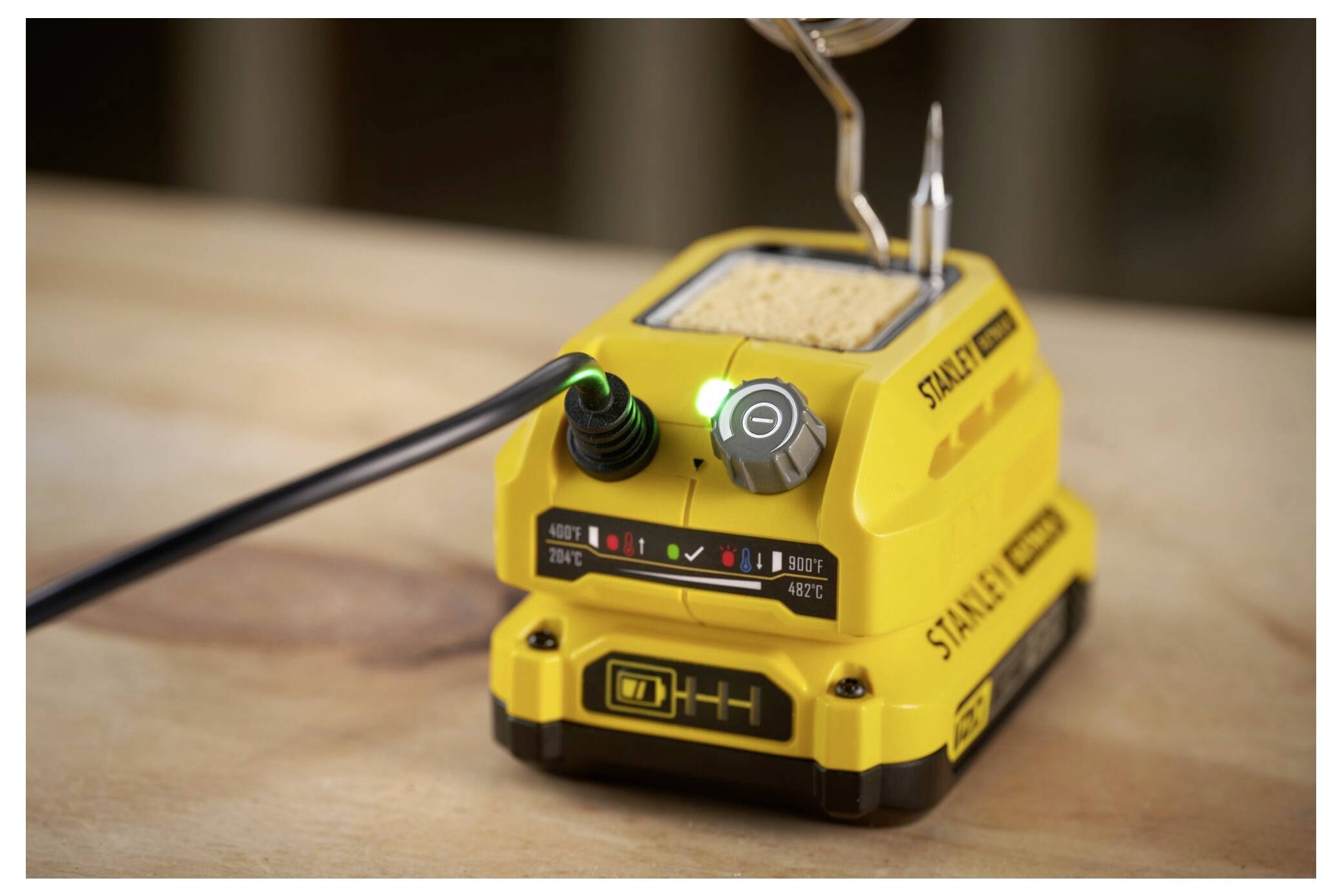A yellow soldering iron station with temperature control and a visible power button, placed on a wooden surface.