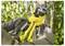 A person using a yellow and black tree branch cutter in a garden. The focus is on the tool cutting a branch among green leaves.