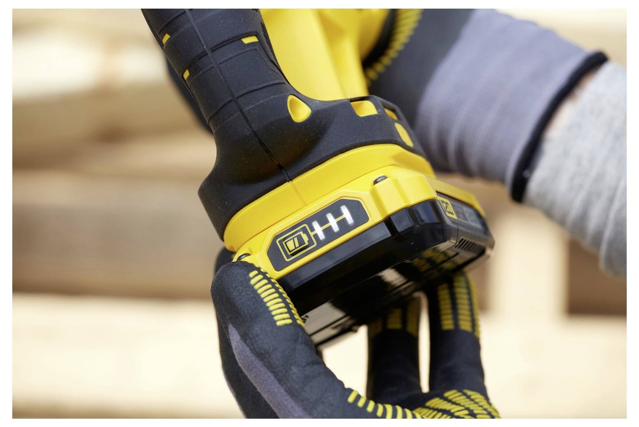 A person wearing gloves inserts a yellow and black battery into a power tool, preparing for use during construction work.