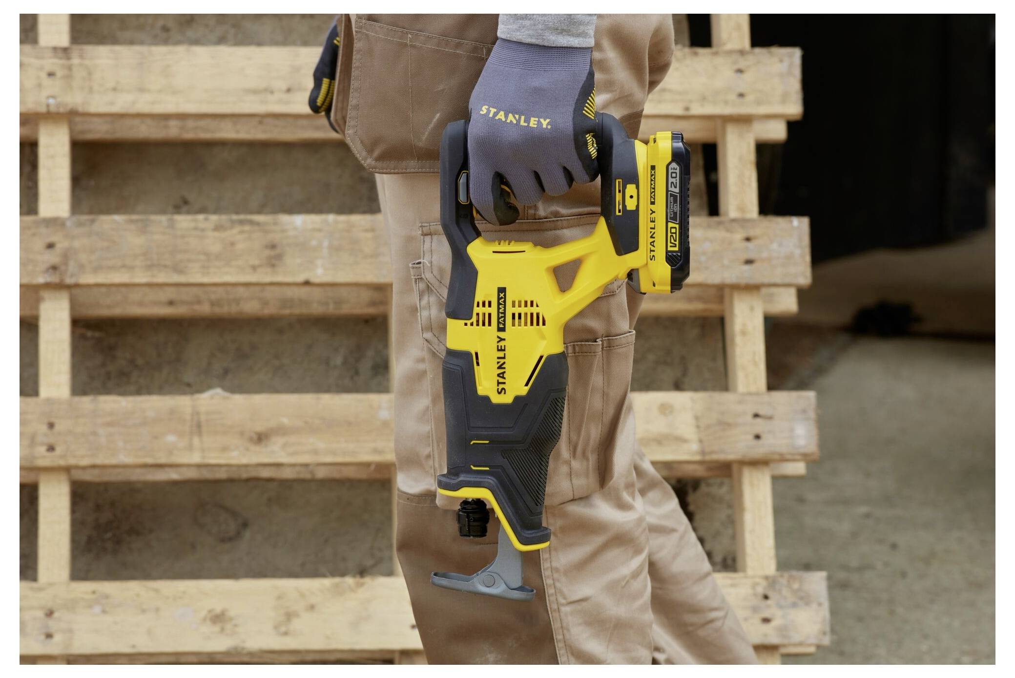 A person wearing gloves holds a yellow and black handheld power tool labeled 'Stanley' in front of wooden pallets.