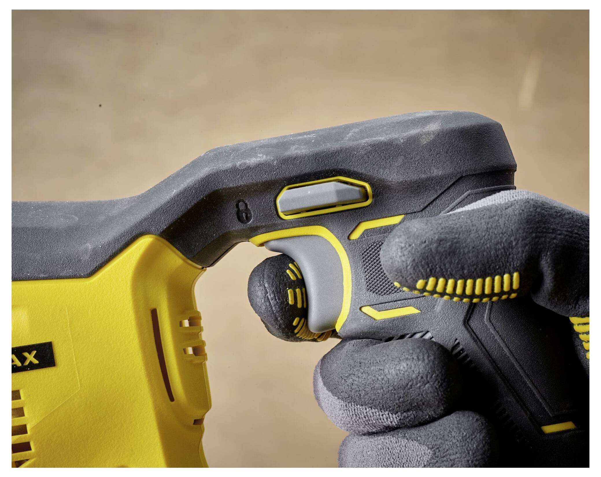 A person wearing gray gloves grips the handle of a yellow power tool, focusing on the trigger and safety lock area.