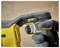 A person wearing gray gloves grips the handle of a yellow power tool, focusing on the trigger and safety lock area.