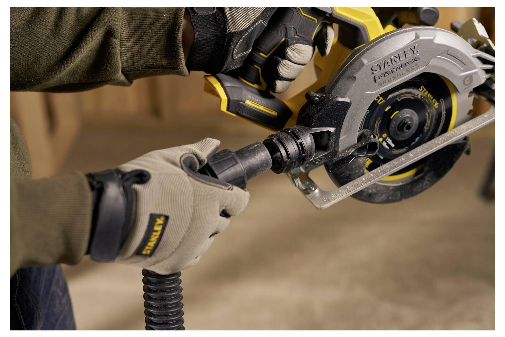 'A person operates a circular saw, wearing gloves and holding a vacuum attachment. The saw is branded Stanley.'