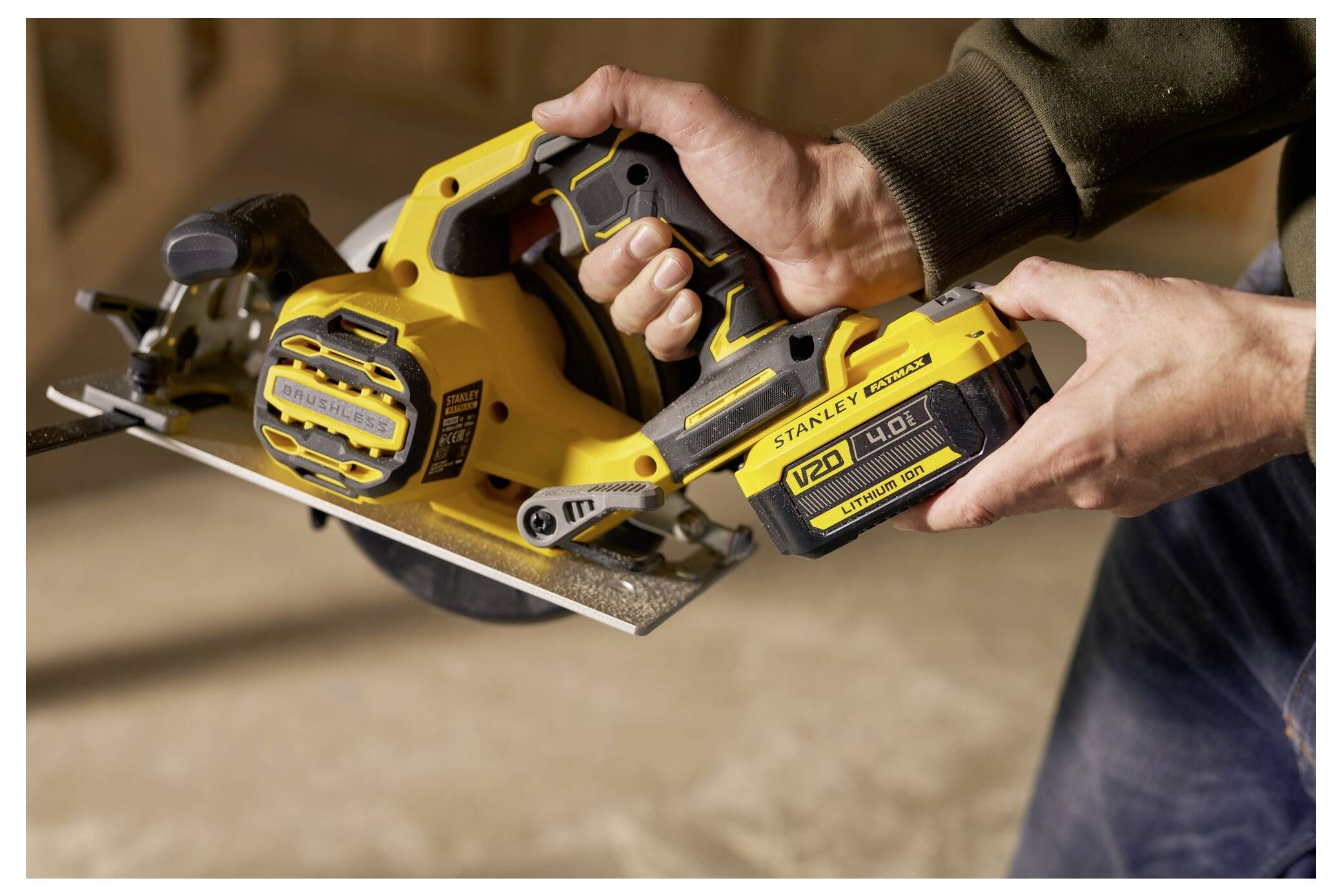 A person holds a yellow and black cordless circular saw, ready to use. The saw is labeled 'STANLEY FATMAX V20'.