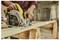 A person uses a circular saw to cut a wooden plank on a workbench in a workshop.