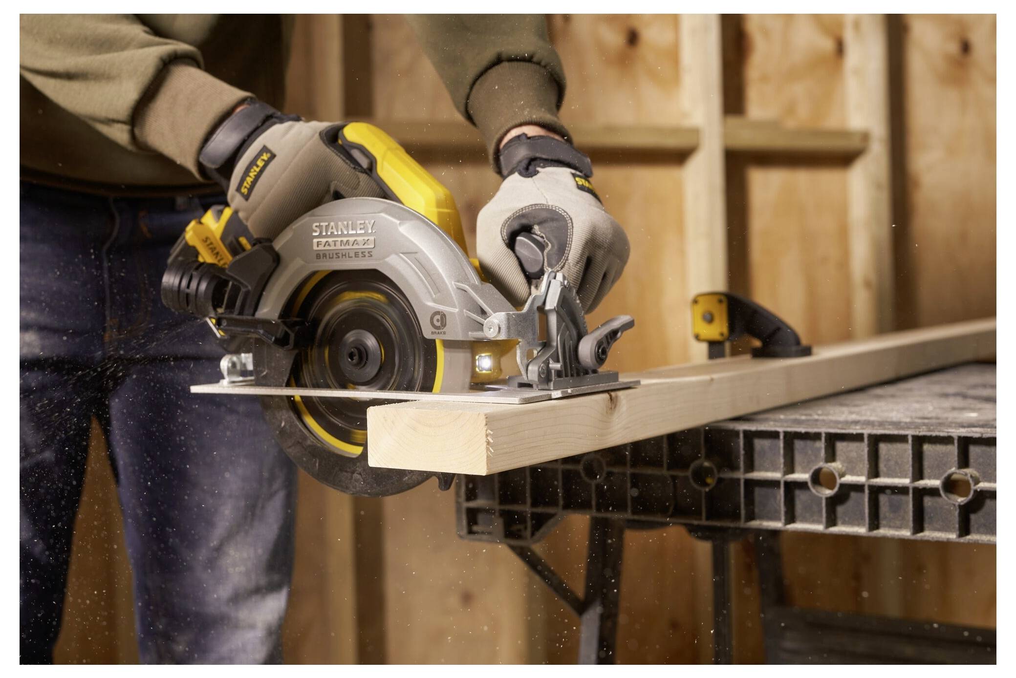 A person uses a circular saw to cut a wooden plank on a workbench, wearing gloves for safety in a workshop setting.