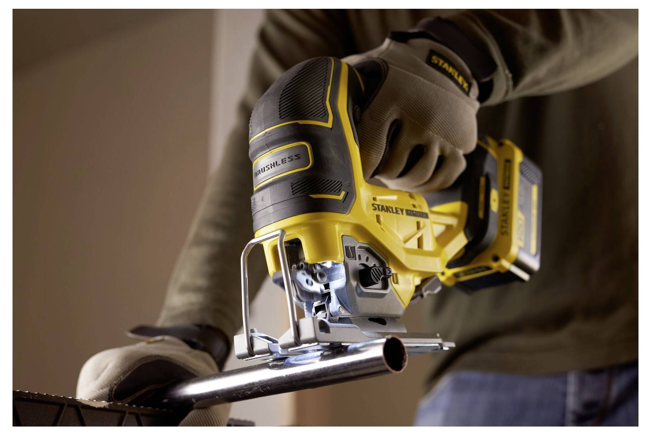 A person wearing gloves uses a yellow power jigsaw to cut a metal pipe, focusing on precision and safety.