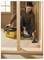 A man in a green hoodie uses a yellow vacuum to clean wood shavings from the floor in a carpentry workshop.
