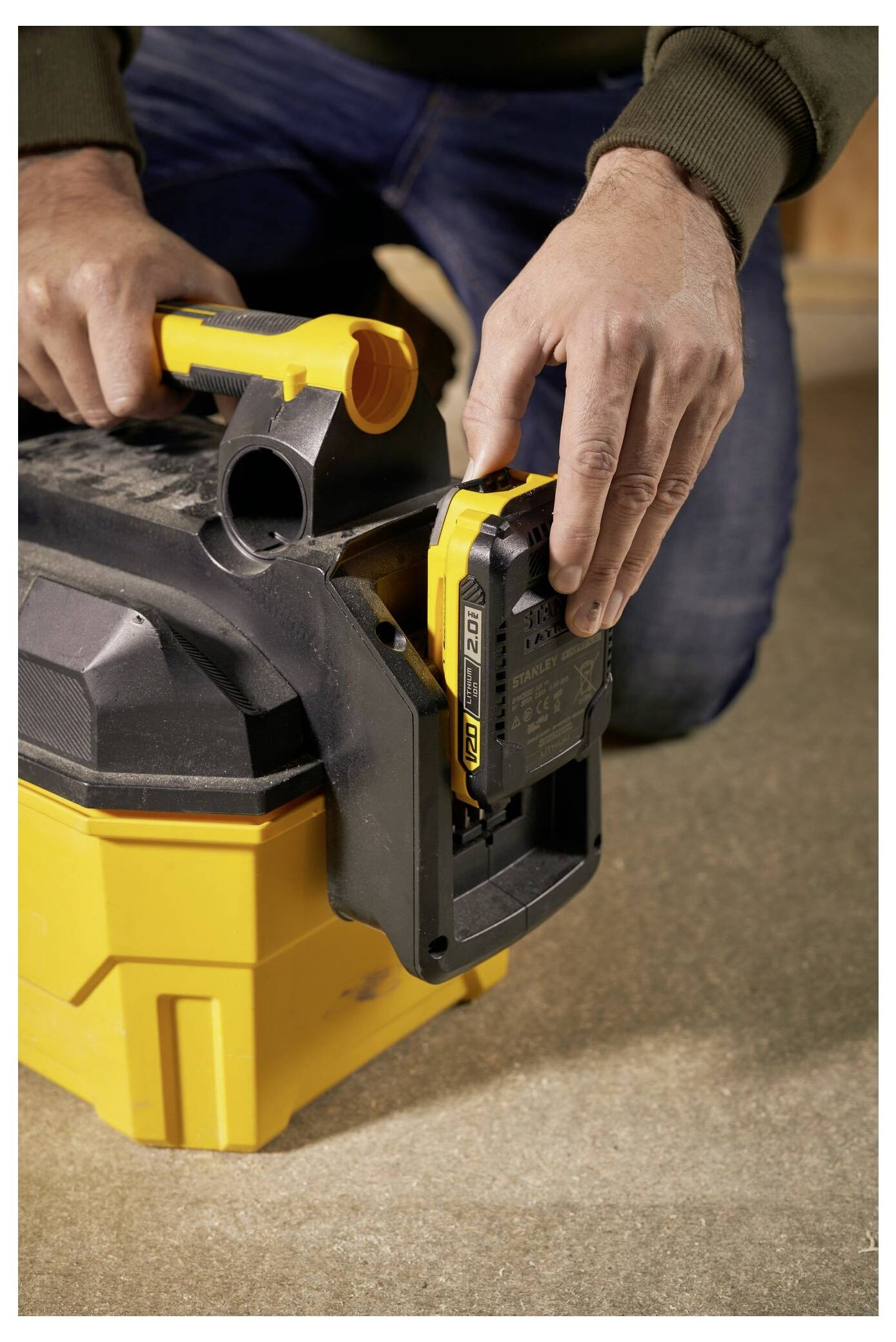 A person demonstrates inserting a battery into a yellow portable vacuum on a brown surface, focusing on the proper alignment and fit.
