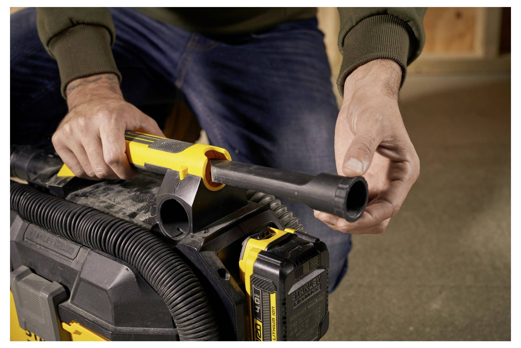 A person connects a hose to a yellow and black vacuum cleaner in a workshop, highlighting the process of attaching parts securely.
