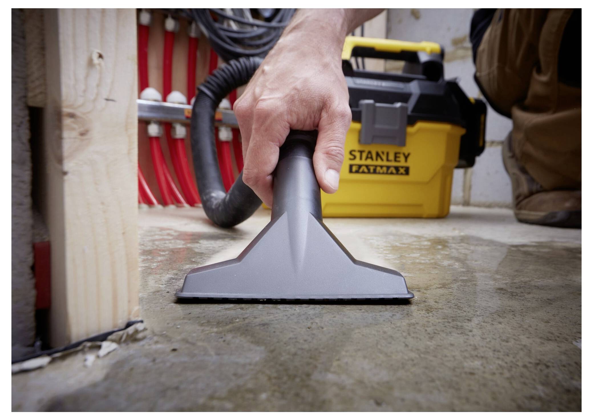A person uses a wet/dry vacuum cleaner to remove water from a concrete floor in a workshop, with tools visible in the background.