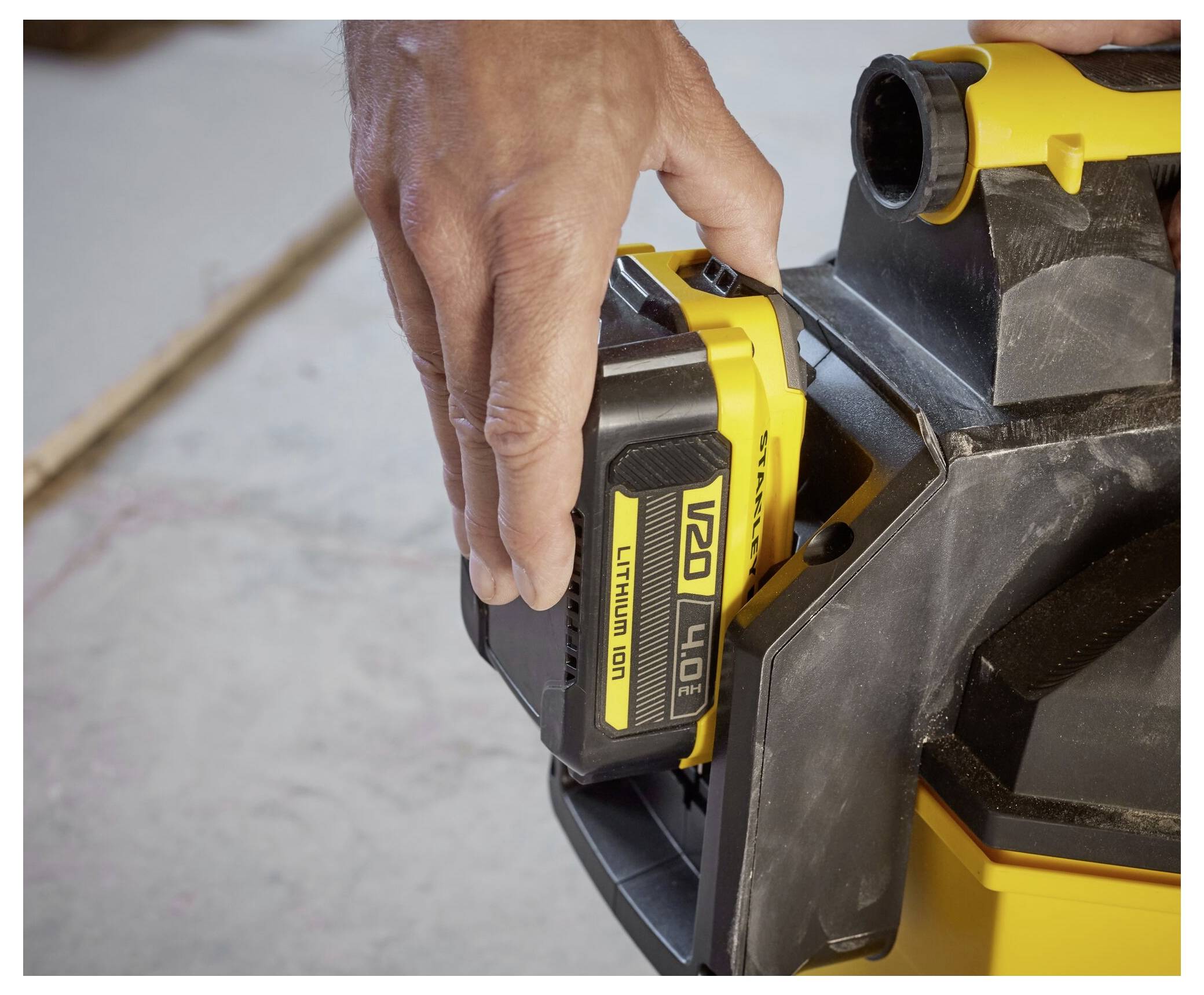 A person inserts a '20V Lithium Ion 4.0Ah' battery into a yellow and black power tool on a concrete floor.