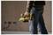 A person holds a yellow power sander in a partially renovated room with exposed electrical outlets in the wall.