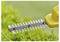 A hedge trimmer with sharp, metal blades in motion, trimming green leaves. The tool is yellow, highlighted against a blurred background of greenery.