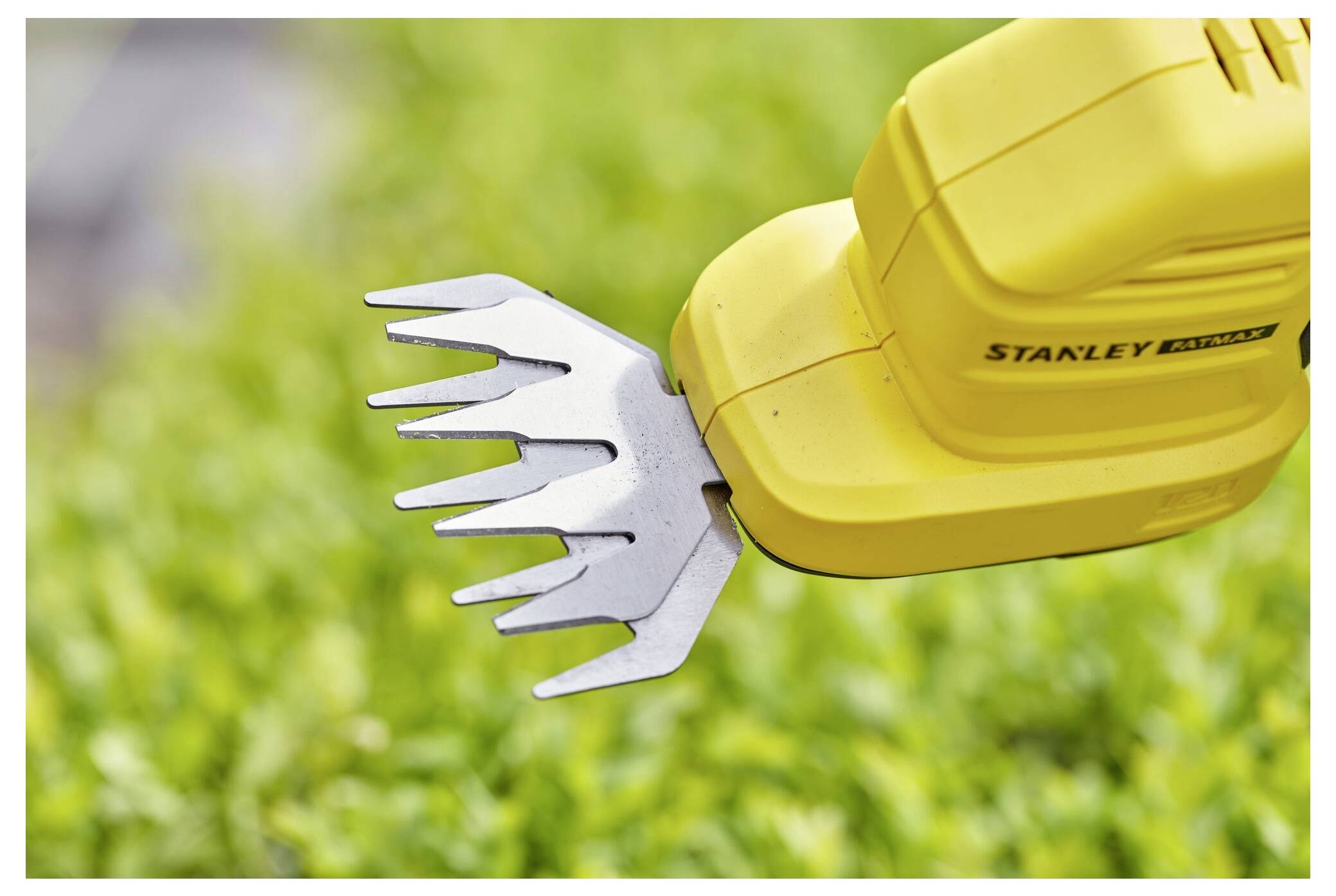A yellow handheld garden trimmer with silver blades is positioned over green foliage, suggesting trimming or pruning activity.