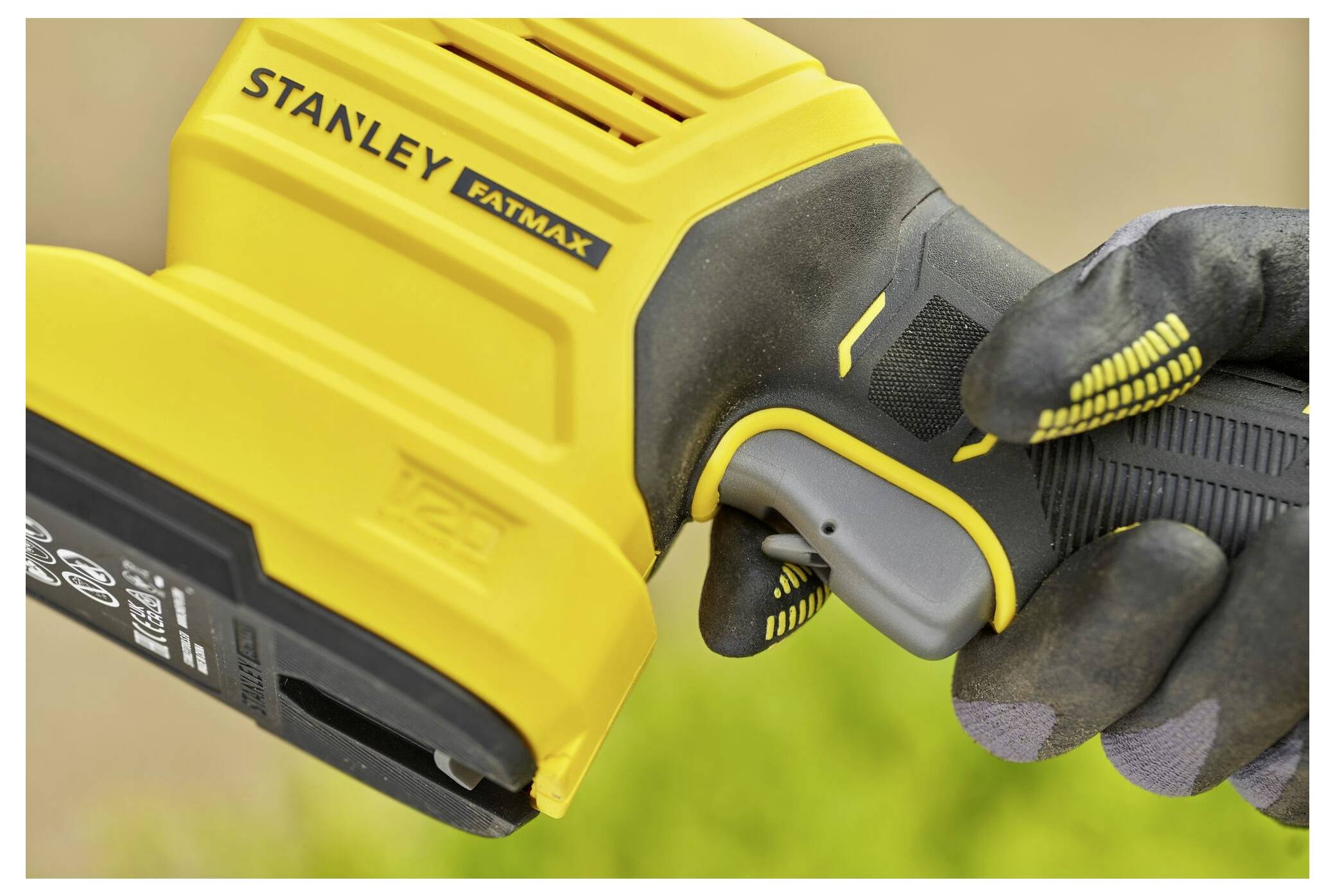 A person wearing gloves holds a yellow and black 'Stanley FatMax' power tool, focusing on the handle and trigger area.