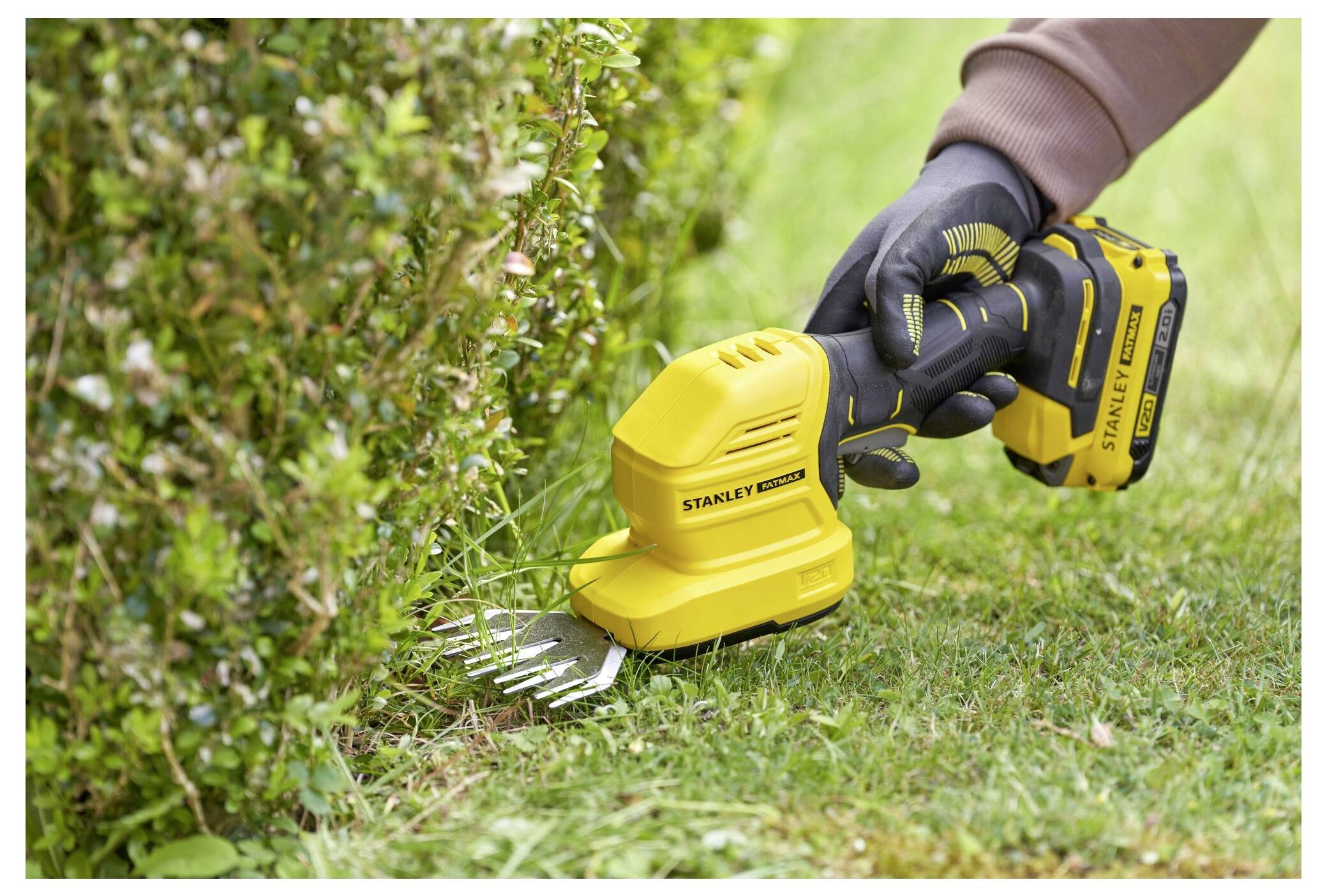 A person uses a yellow handheld hedge trimmer to neatly trim the edges of a green shrub, showcasing precise gardening work.