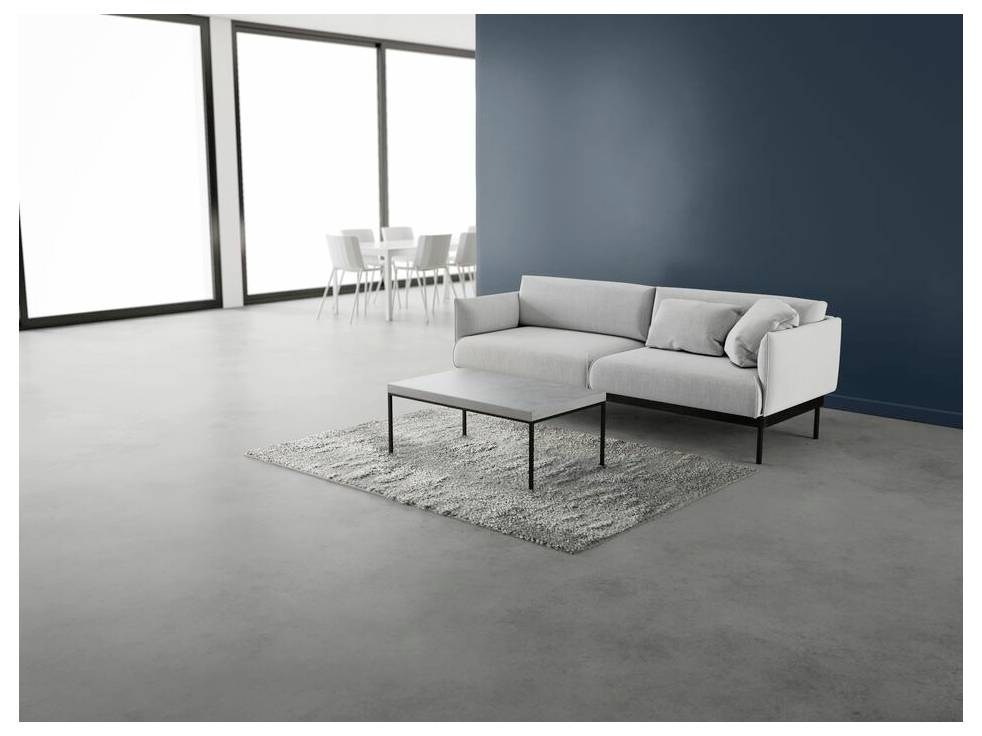 A modern living room with a white sofa facing a dark blue wall, a matching coffee table on a light gray rug, and a dining area in the background.