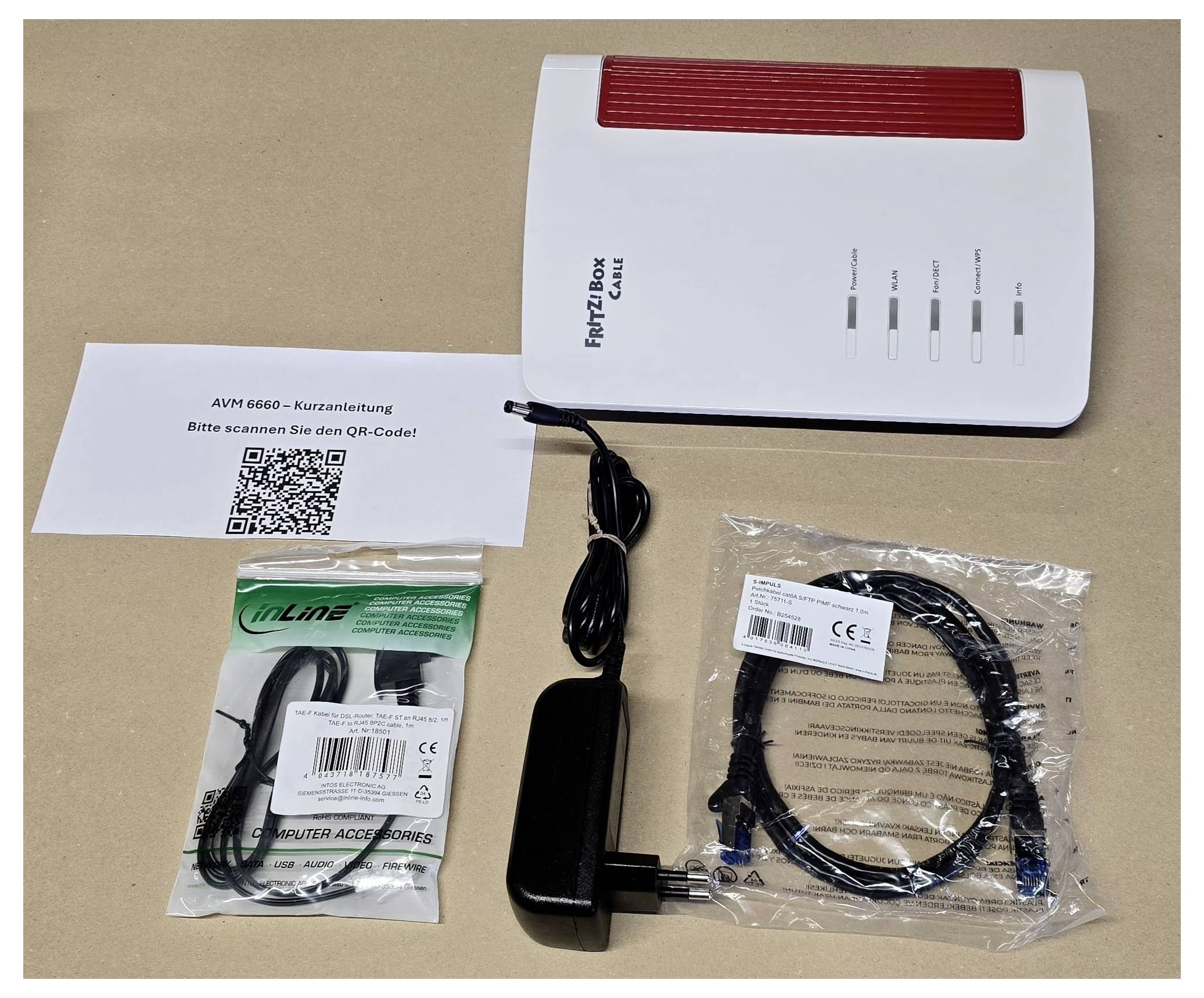 A router with a red top labeled 'FRITZ!Box', two cables, a small antenna, and a QR code.