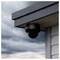 A security camera mounted under the eaves of a building during rainy weather, with a cloudy sky in the background.