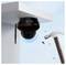 A security camera installed under a roof corner is being struck by a hammer, with pieces flying off, showcasing an impact-resistant feature.