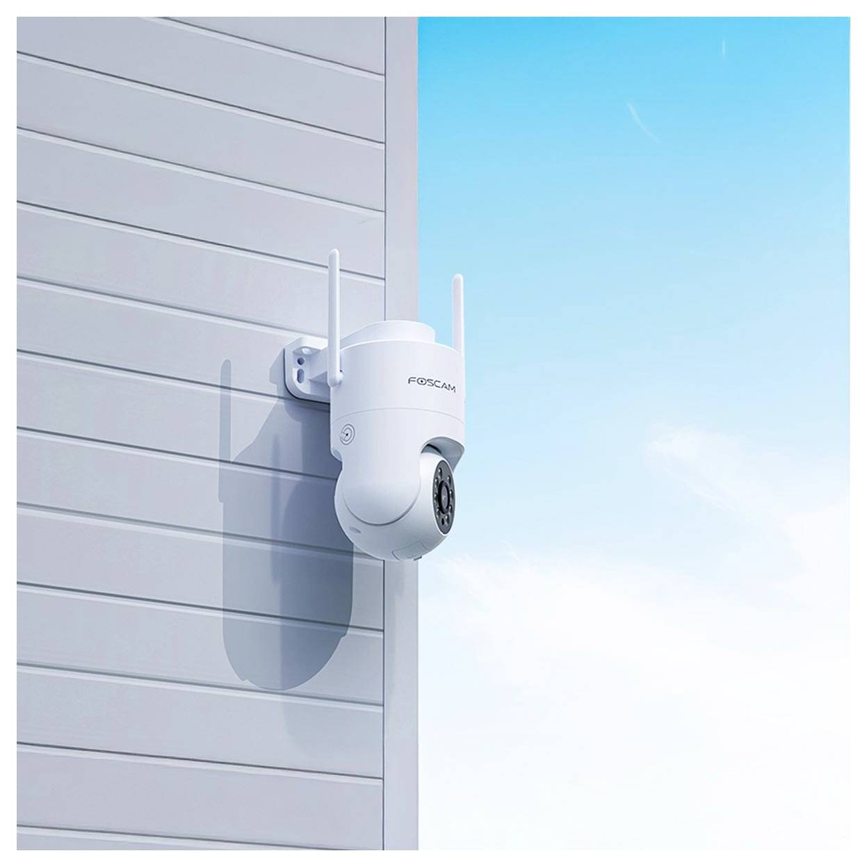 A white security camera with antennas is mounted on a light gray wall under a clear blue sky.