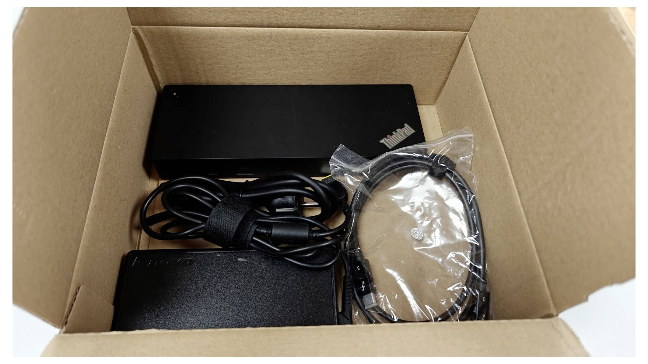 A cardboard box containing a black electronic device, power adapter, and cables, neatly arranged for shipping or unpacking.