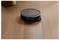 A round robotic vacuum cleaner on wooden flooring, navigating autonomously near a furniture leg.