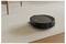 A black robotic vacuum cleaner on a carpet, next to a wooden furniture piece. It is cleaning autonomously in a home environment.