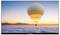 A hot air balloon soars above a cloud-covered landscape at sunrise, with distant mountains on the horizon.