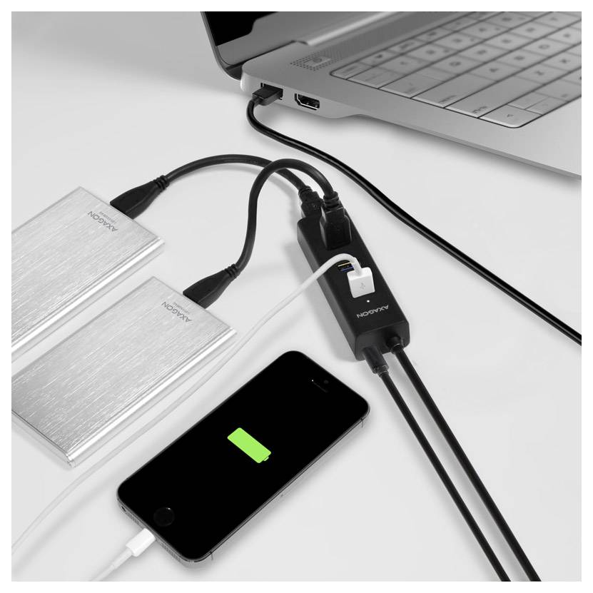 Laptop powers two external drives and charges a smartphone through a multiport hub on a desk.