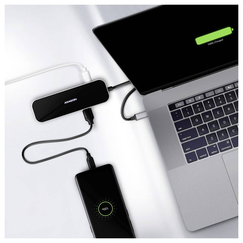 Laptop connected to a USB-C hub and charging smartphone on a white desk, showing an ongoing battery charge on both devices.