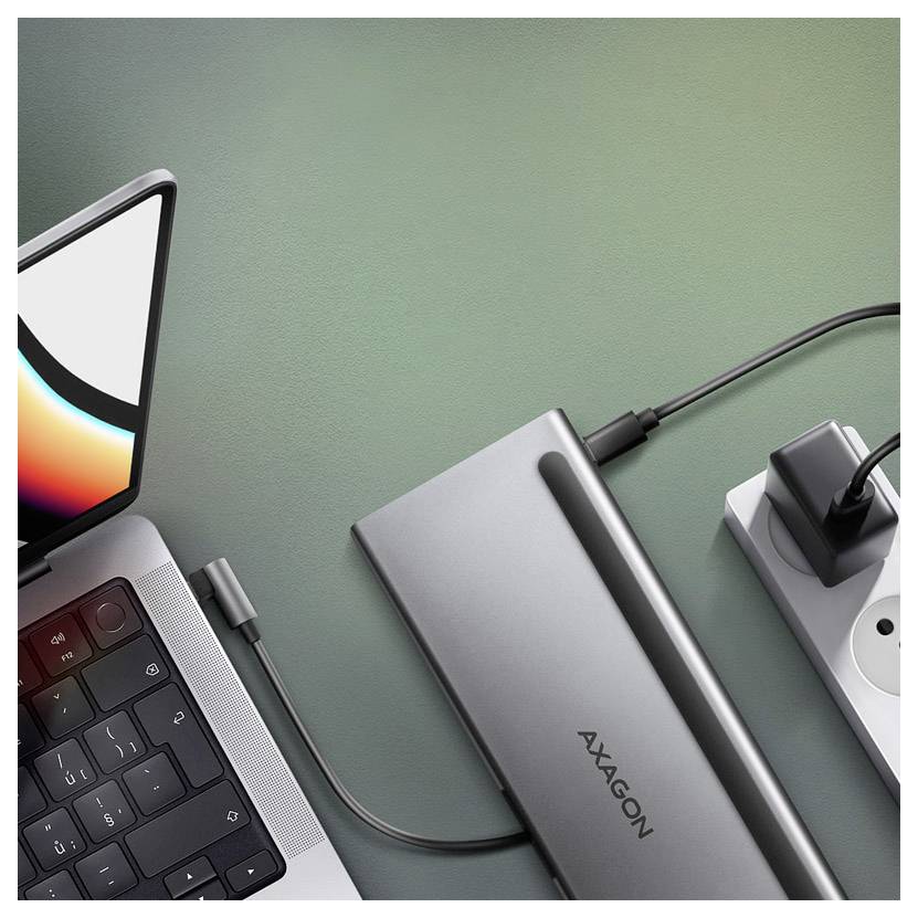 Laptop connected by cable to an AXAGON external drive and power strip on a green desk, showing a charging/data setup.