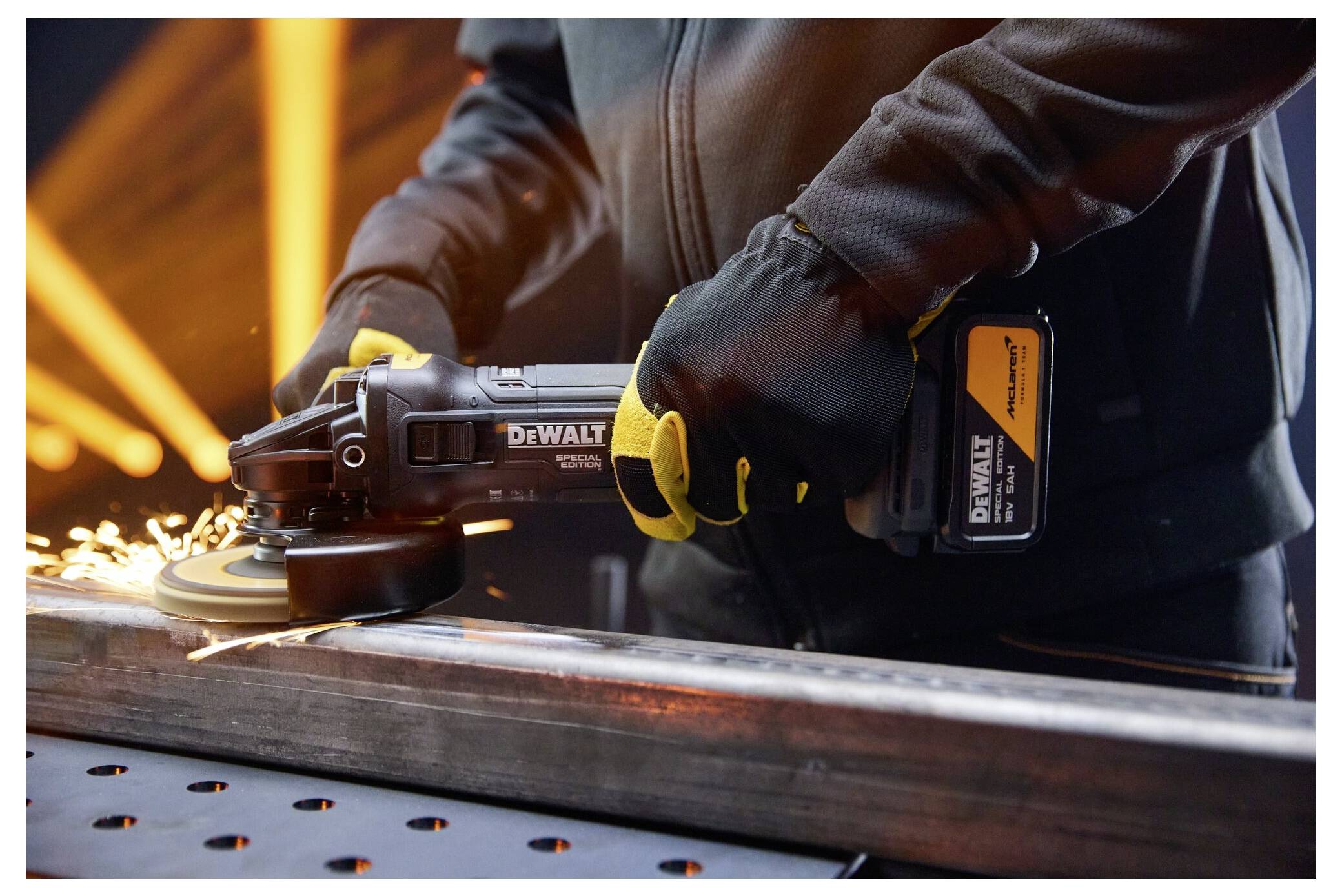 Worker using a DeWalt angle grinder to cut a metal beam, with sparks flying in a workshop.