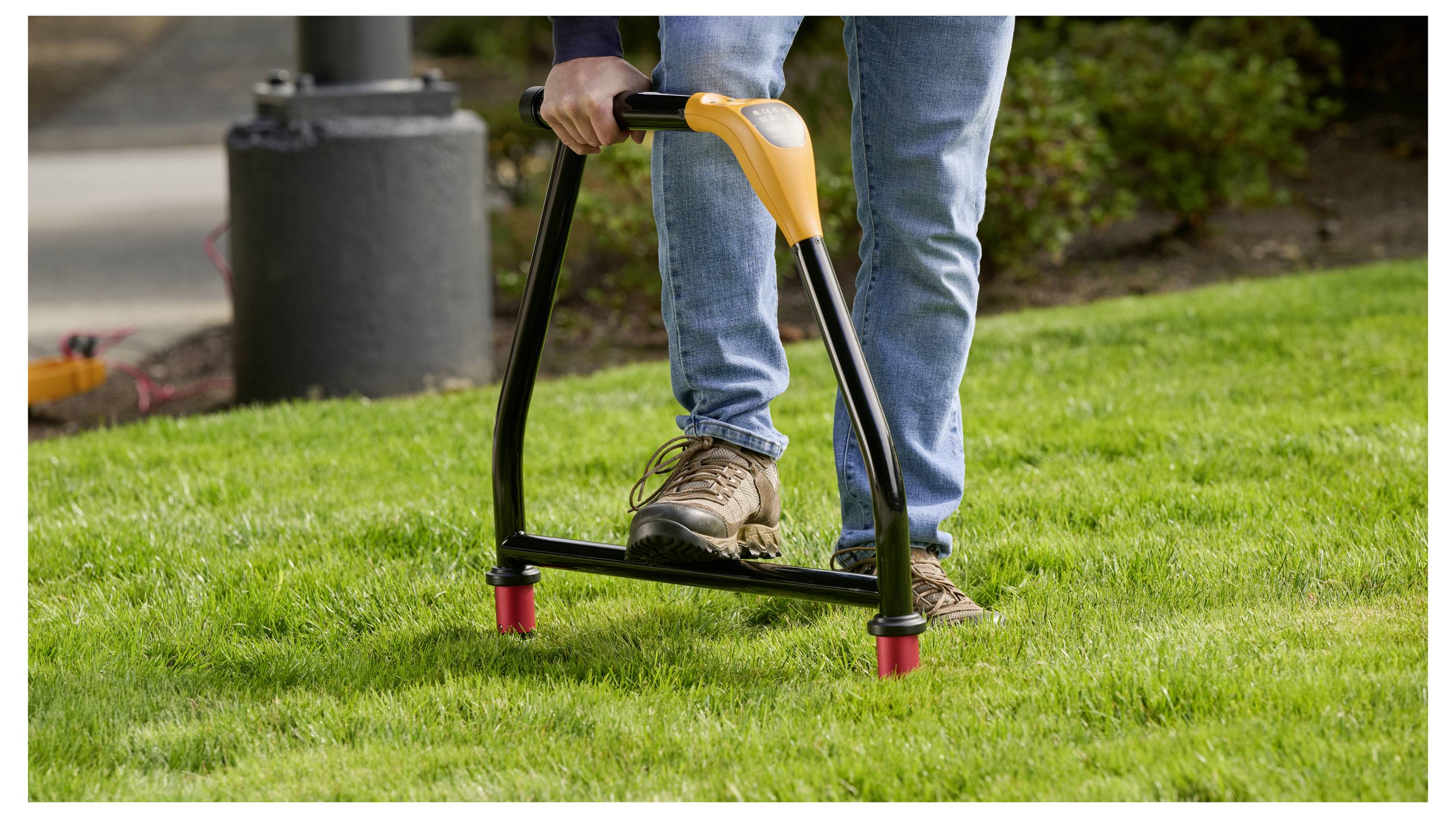 Person using a black-and-orange lawn aerator tool on a grassy yard.