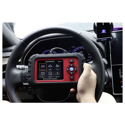 Handheld AUTOPHIX car diagnostic scanner showing a multi-system menu, held in front of a vehicle steering wheel inside a car.<br>