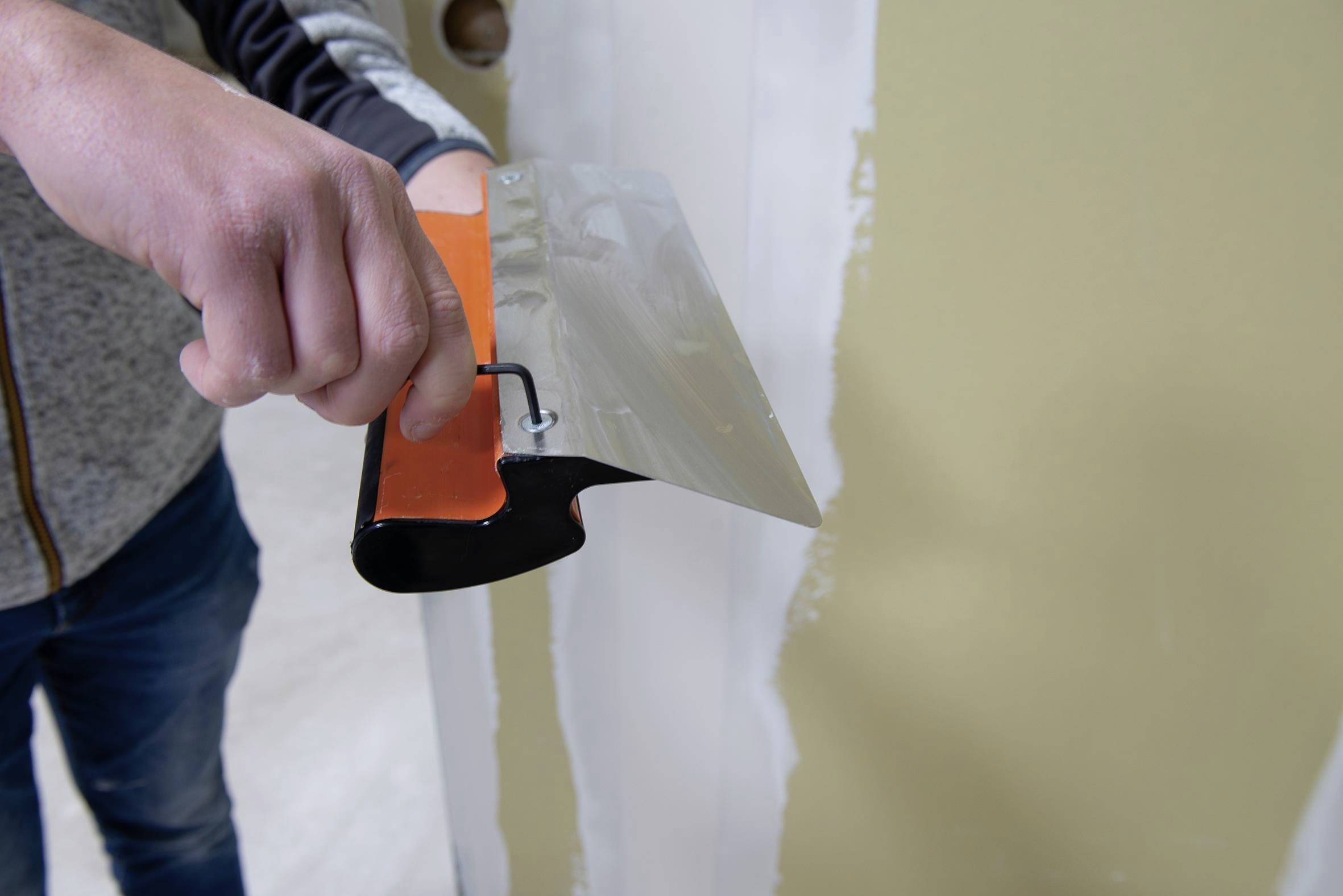Person applying joint compound to a wall with a putty knife during drywall repair<br>