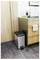 Kitchen corner with a stainless steel trash can beside wood cabinets and a countertop holding a coffee press, grapes, and vegetables.