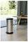 Stainless steel kitchen trash can on a wooden floor beside a dining table set with vegetables and a bottle, near a sliding glass door.