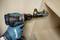 Gloved hand uses a Makita cordless drill to install a cabinet hinge inside a wooden cabinet.