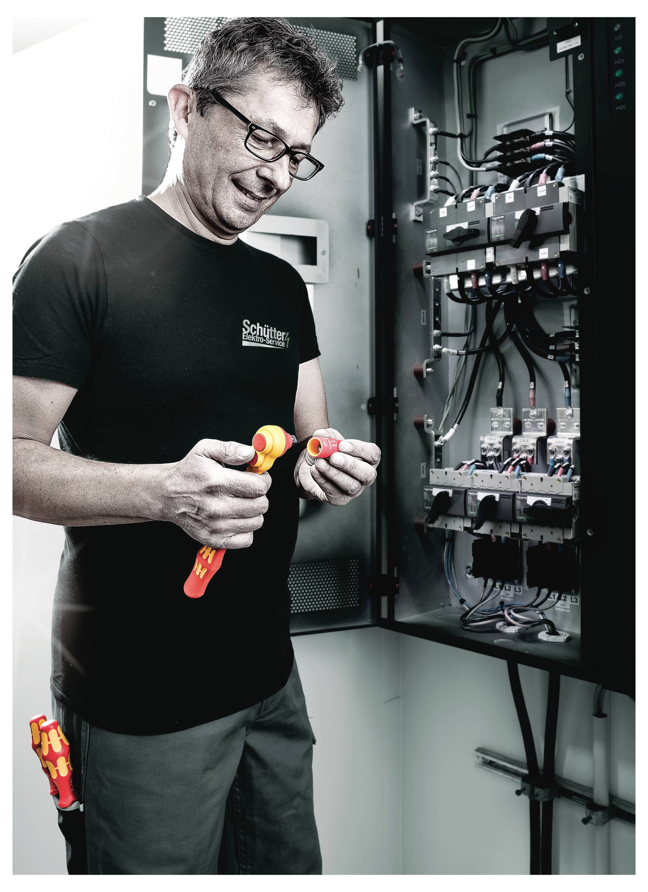 Technician in a server or electrical cabinet inspects and handles wiring tools inside an open control panel.<br>