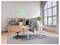 Modern open office with standing desks, monitors, stools, shelving, and a neon 'FEEL GOOD' sign beside large arched windows.
