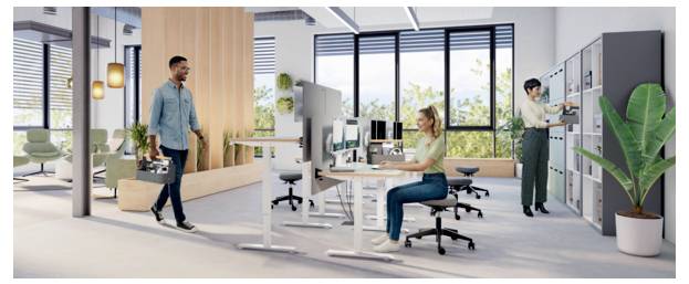Modern open-plan office with a man carrying a briefcase walking past a seated woman at a desk, computers, partitions, and storage cabinets.