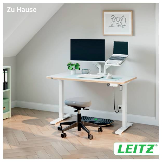 Home office setup with adjustable standing desk, monitor, laptop, stool, and accessories in a bright attic room; LEITZ branding.