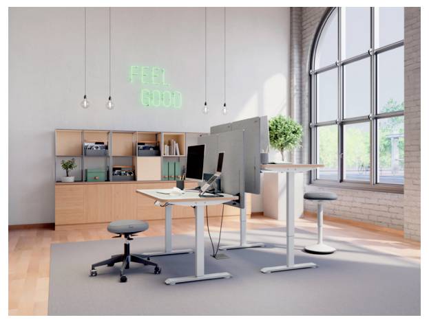 Modern bright office with standing desks, monitor, stool, shelving, and neon 'FEEL GOOD' sign by large arched window.