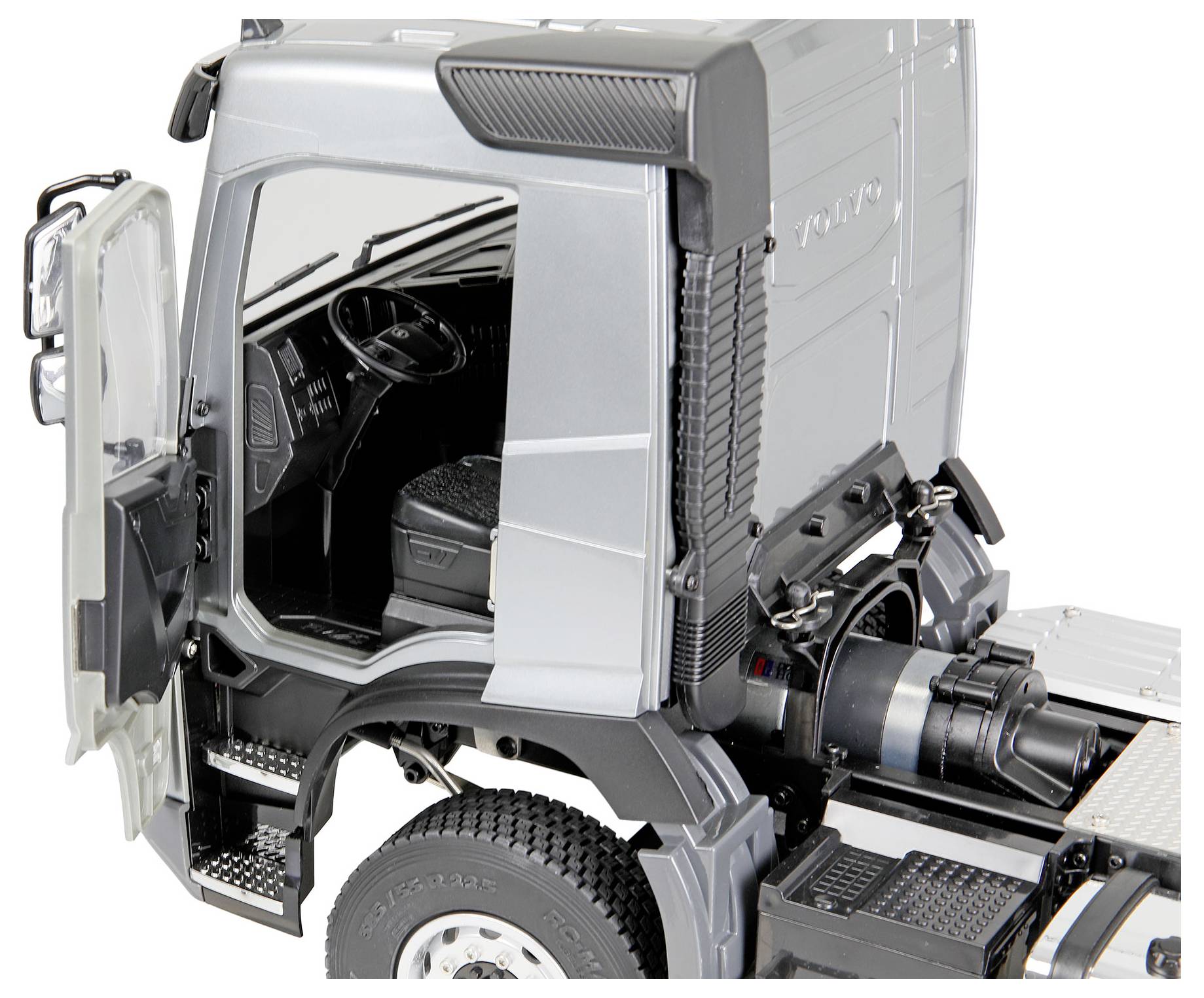 Cutaway view of a gray Volvo truck cab chassis, showing the open door, driver seat, steering wheel, and exposed rear engine components.