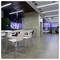 Modern office lounge with white chairs and tables in a bright open corridor, polished floor, glass walls, and seating area in the distance.