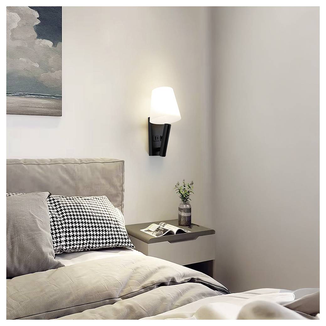 Cozy bedroom corner with an unmade bed, wall lamp, bedside table, and small plant beside a framed seascape print.